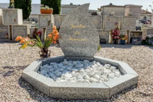 Monument en granit au cimetière, marqué "Jardin du Souvenir" et entouré de galets.