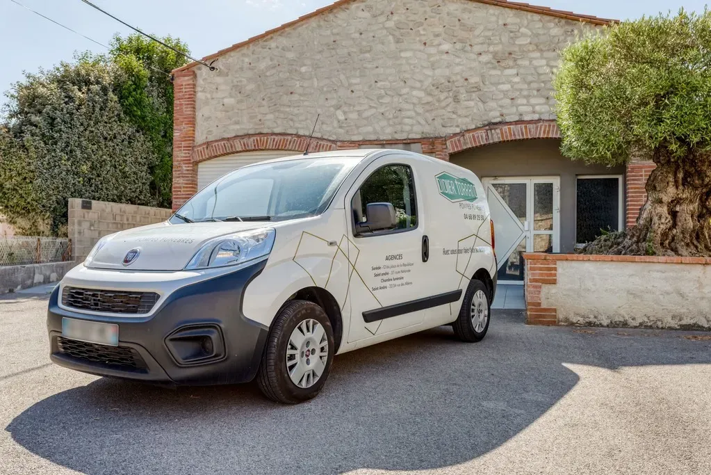 Un petit fourgon blanc utilitaire de l'agence de pompes funèbres garé en extérieur.